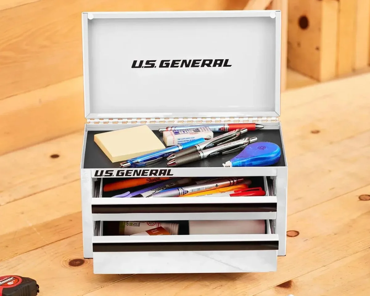 White U.S. General metal toolbox with open lid and drawers filled with pens and office supplies.