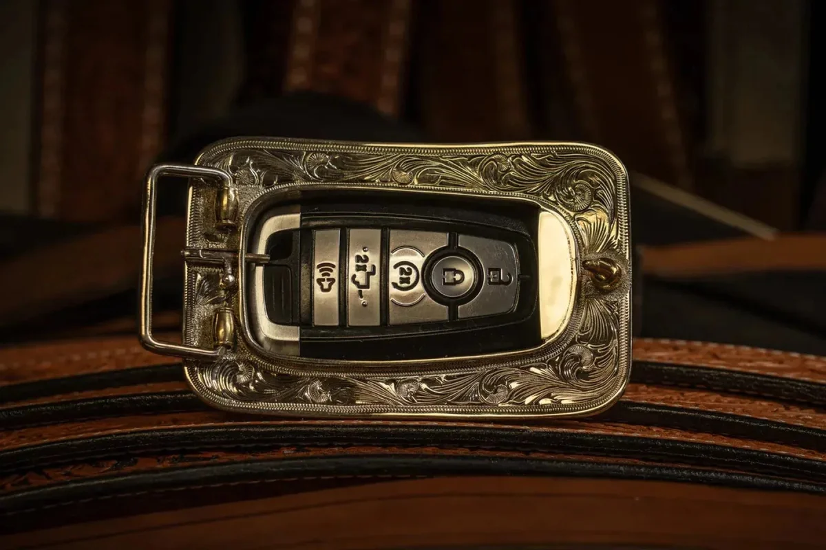 Black car key fob inside a rectangular, ornate silver-toned belt buckle on a brown leather belt.