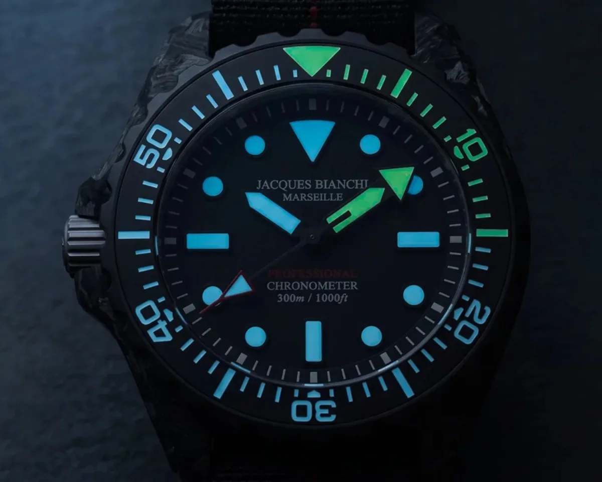 Black Jacques Bianchi Marseille dive watch with glowing blue and green markers and bezel on a dark background.