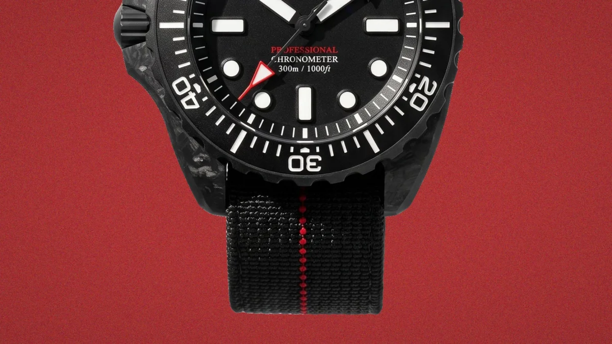 Black dive watch featuring a patterned case, a black dial with luminescent markers, a red-tipped second hand, and a black fabric strap with a central red stripe.