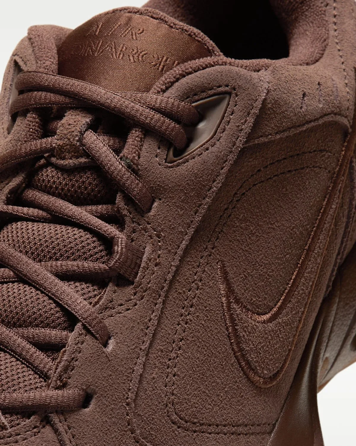 Brown Nike Air Monarch sneaker in a close-up view, featuring a suede upper, mesh tongue, and tonal embroidered swoosh.
