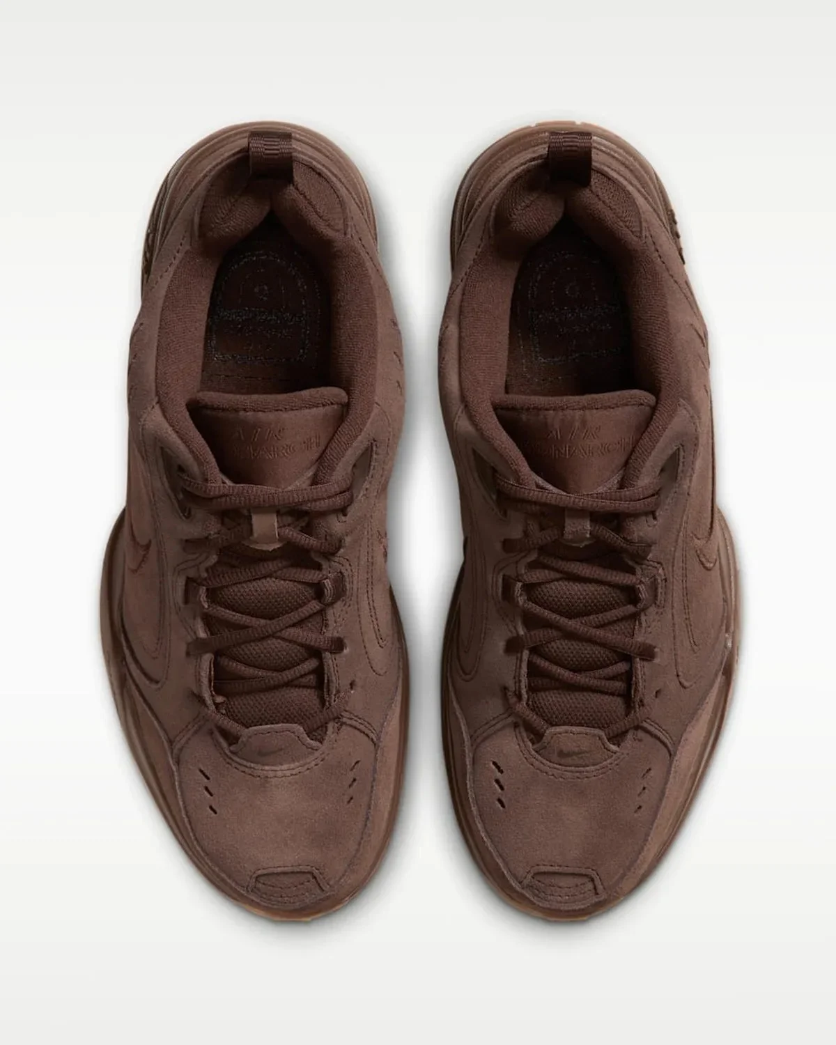 Monochromatic dark brown Nike Air Monarch sneakers, seen from a top-down perspective.