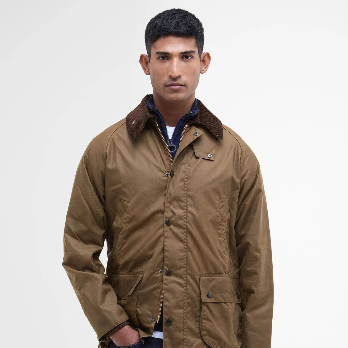 Brown Barbour wax jacket with a corduroy collar and buttoned pockets, layered over a navy zip-up sweater.