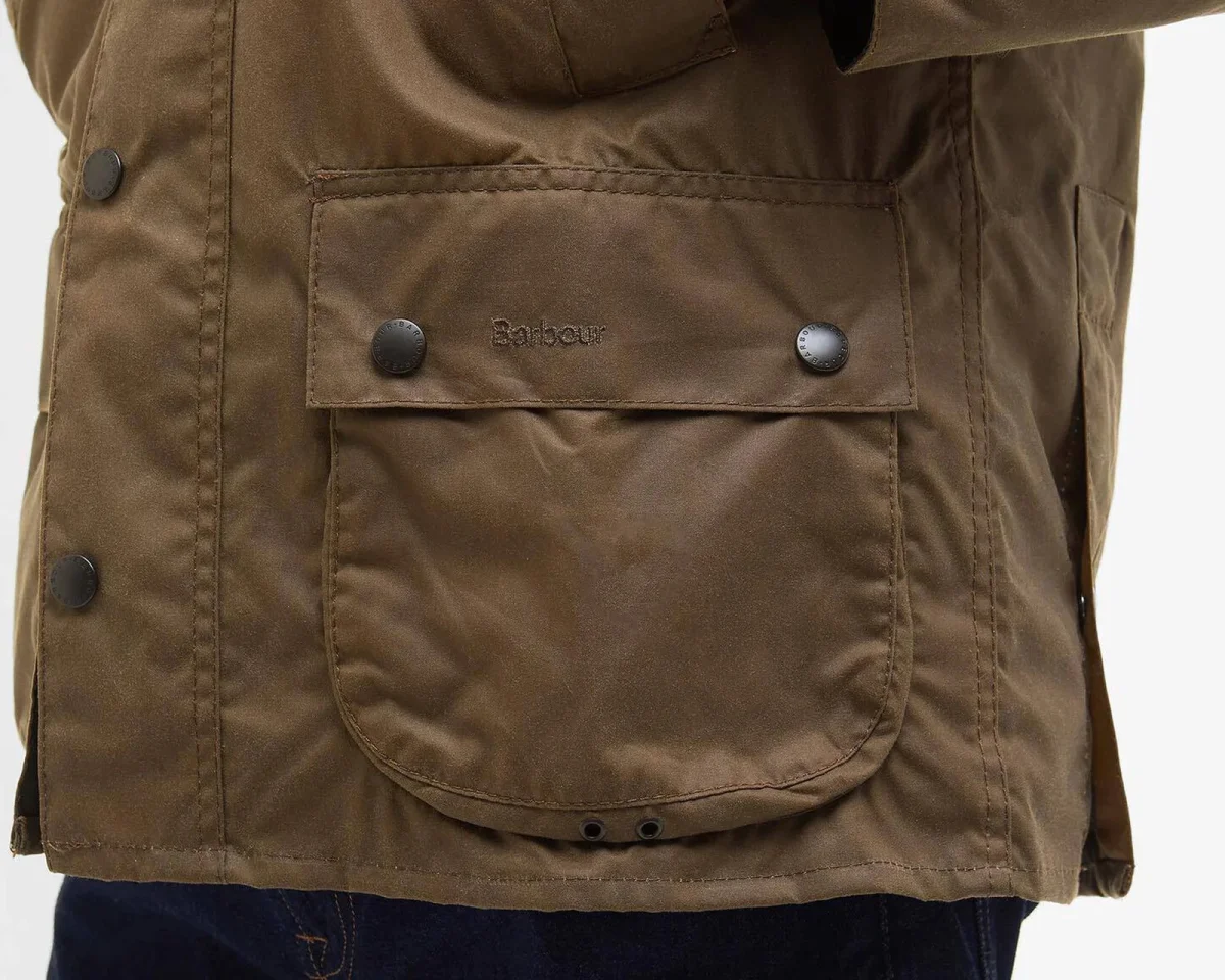 Olive green waxed cotton jacket featuring a large front bellows pocket, Barbour logo, and branded snap buttons.