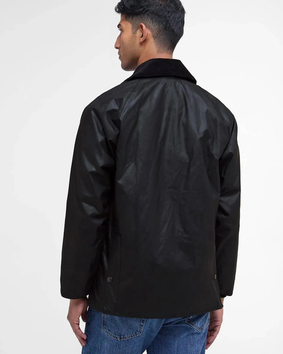 Back view of a black waxed jacket with a corduroy collar and blue jeans.