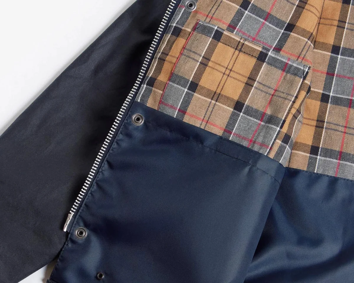 Interior detail of a navy blue jacket featuring a tan, black, and red plaid lining, a metal zipper, and snap closures.