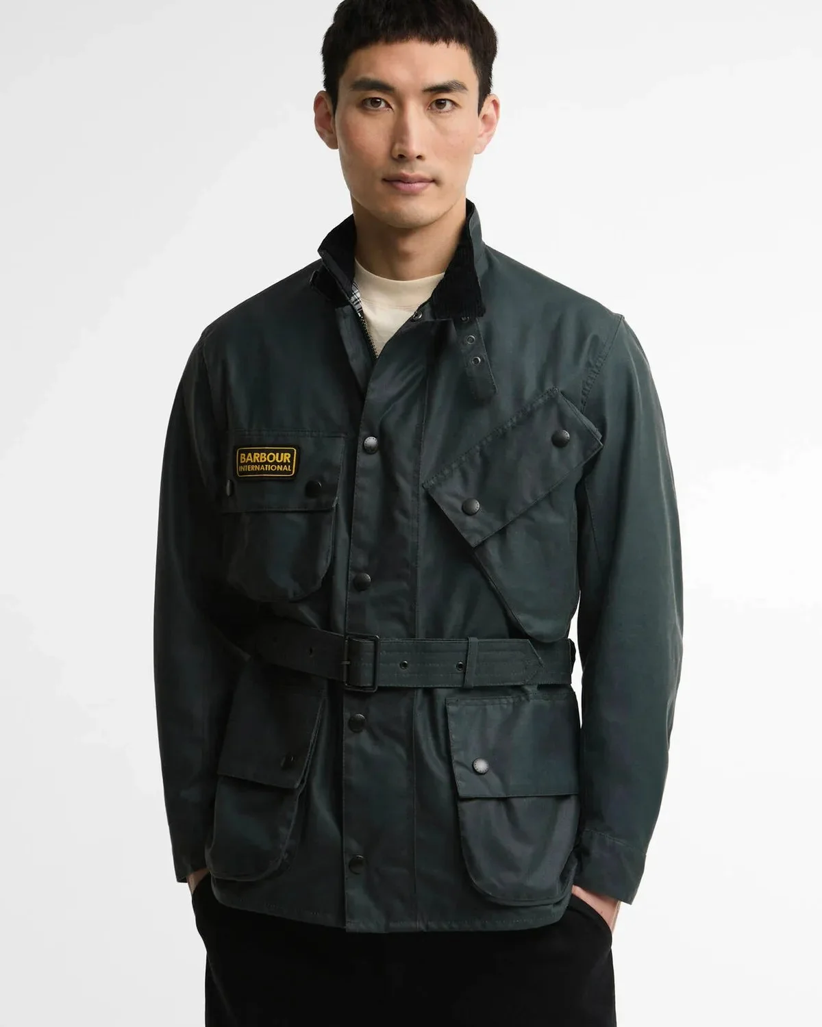 Dark green Barbour International belted wax jacket featuring four front pockets and a yellow brand patch on the chest.
