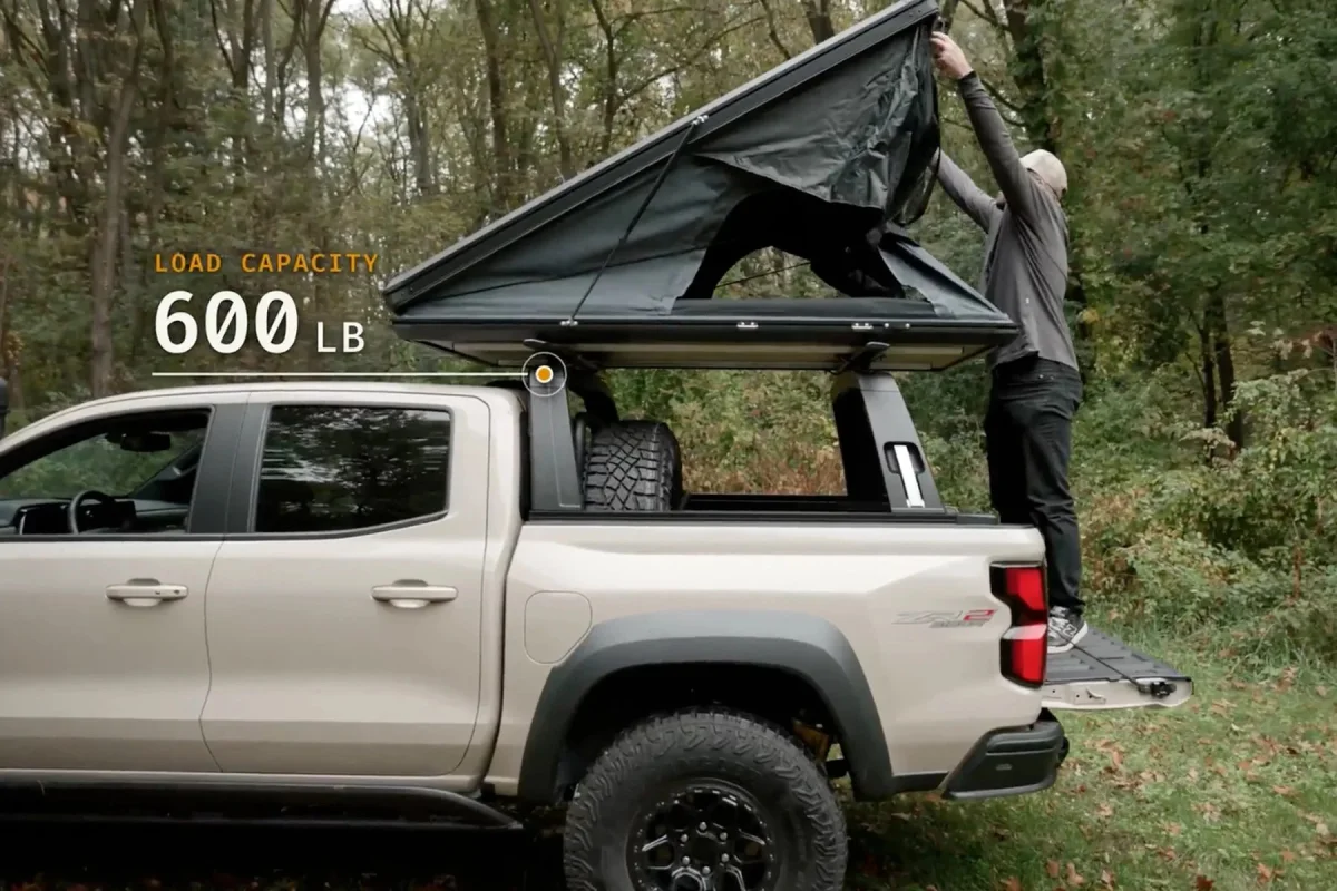 A roof-top tent mounted on a truck bed being set up from the tailgate, with text overlay stating LOAD CAPACITY 600 LB.