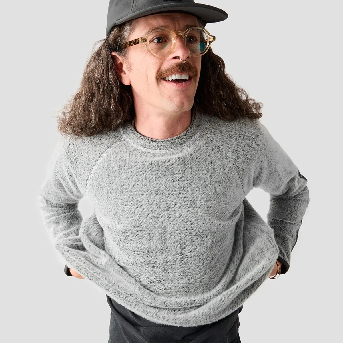 Grey textured sweatshirt, dark cap, and round tortoiseshell glasses.