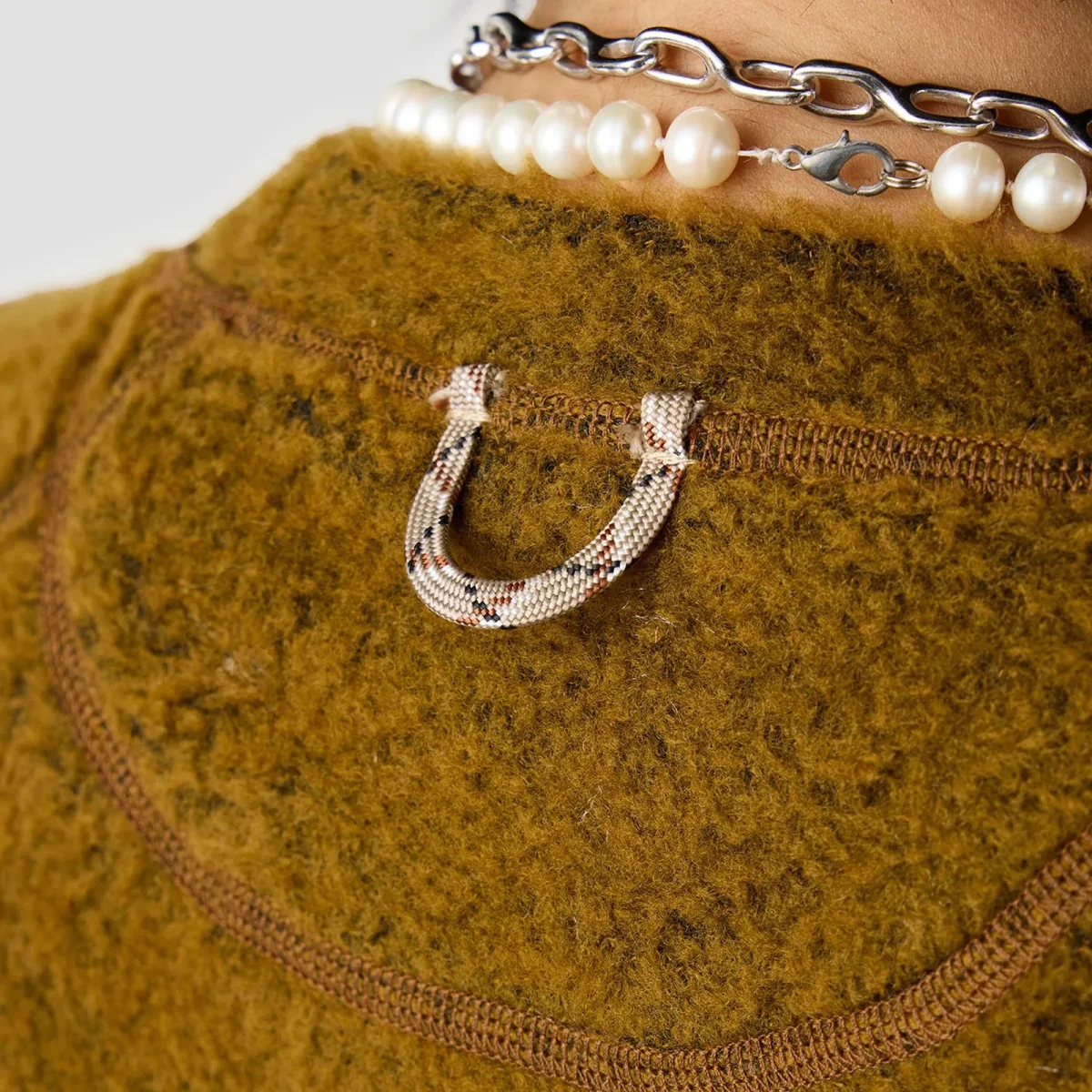 Mustard-brown fuzzy sweater, back view, featuring a patterned cord loop at the neckline and a layered pearl and silver chain necklace.