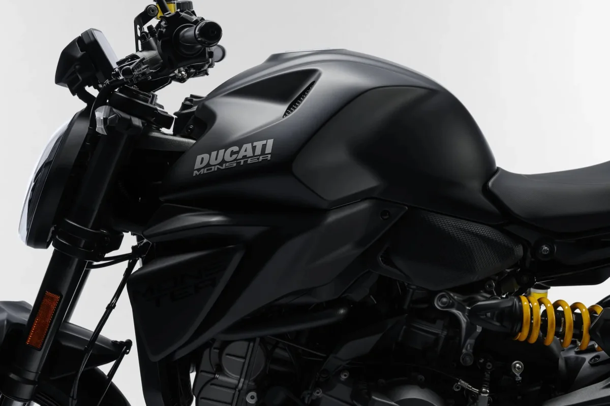 Matte black Ducati Monster motorcycle featuring prominent fuel tank branding and a yellow rear suspension spring.