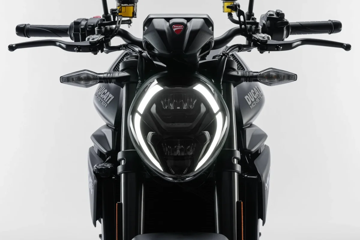 Front view of a matte black Ducati Monster motorcycle featuring an oval LED headlight with a signature light ring and branded tank decals.