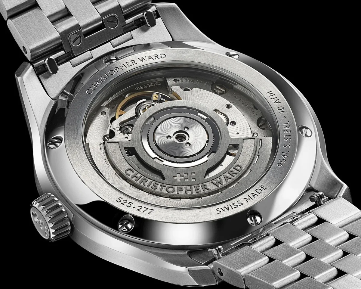 Exhibition case back of a Christopher Ward watch featuring an internal mechanical movement, engraved steel casing, and a metal link bracelet.