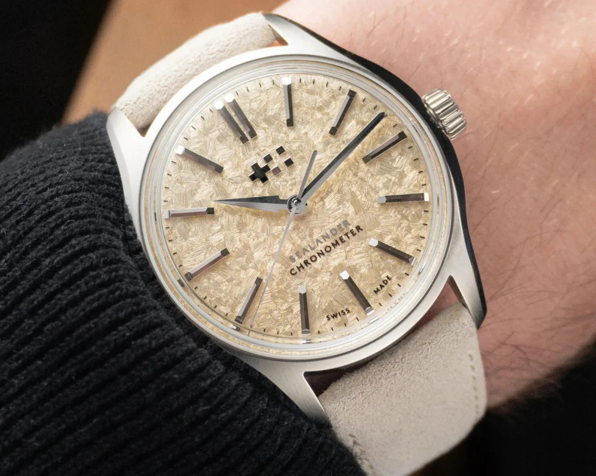 Christopher Ward Sealander Chronometer watch with a textured champagne dial and off-white suede strap, worn on a wrist.