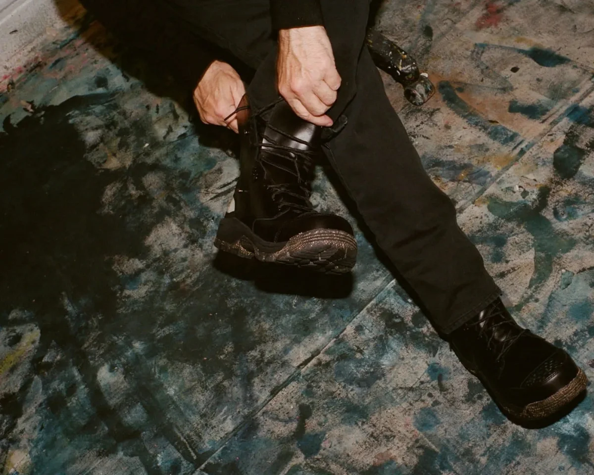 Hands tying the laces of a black, high-top, lug-sole boot.