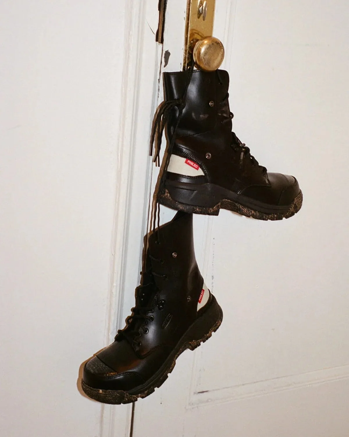 Two black lace-up boots with mud-caked soles hanging from a door handle.
