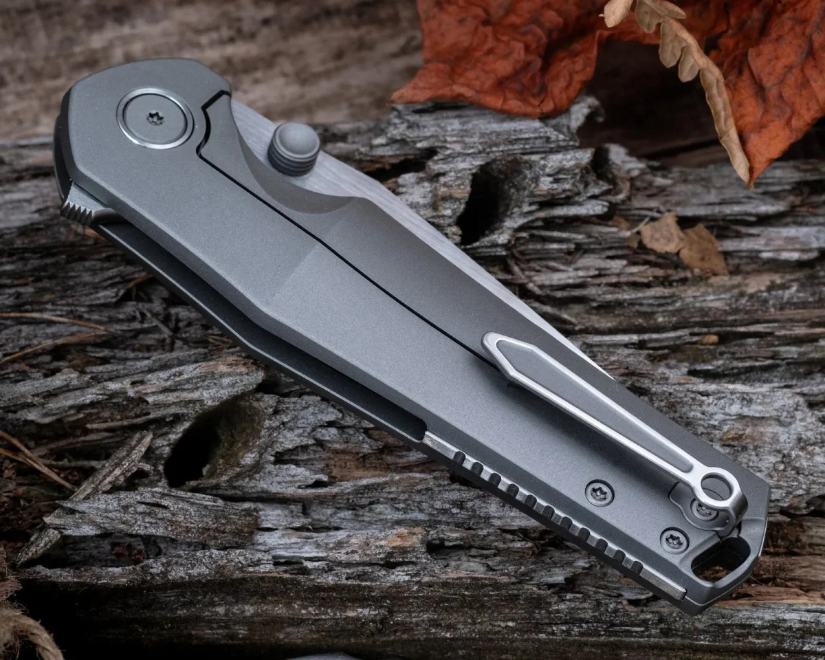 Folding knife with a gray metal handle and a pocket clip, resting on weathered wood.