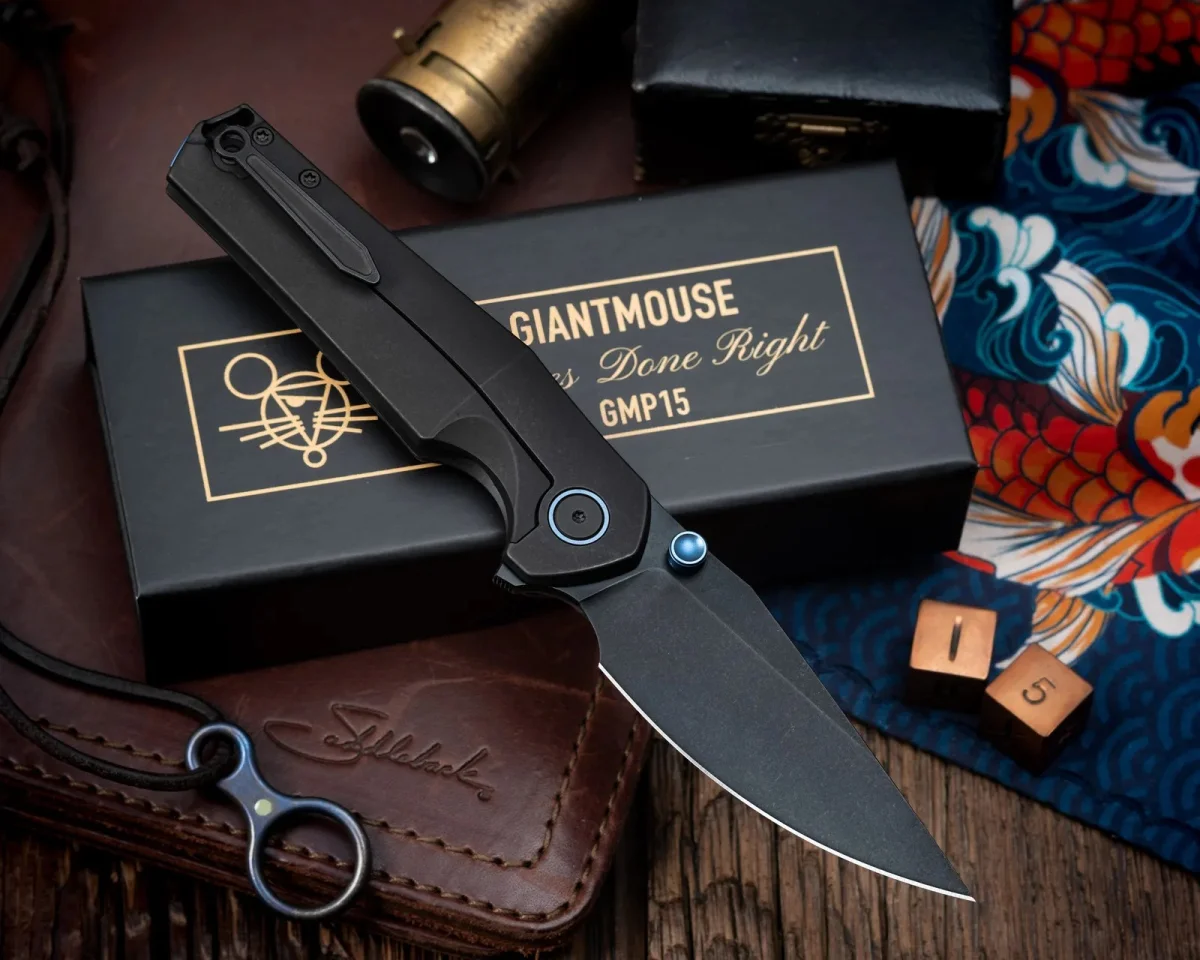 Black GiantMouse folding knife featuring a blue pivot collar and thumb stud, positioned on its branded black box.