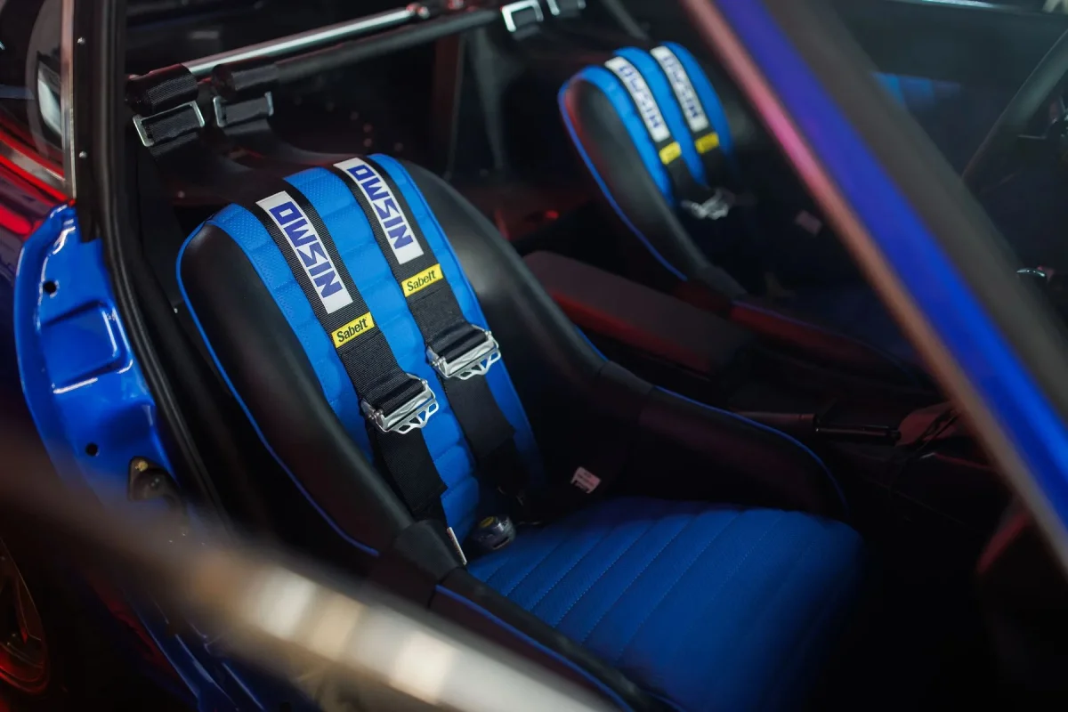 Blue and black racing bucket seats featuring Nismo harness straps, installed inside a vehicle interior.