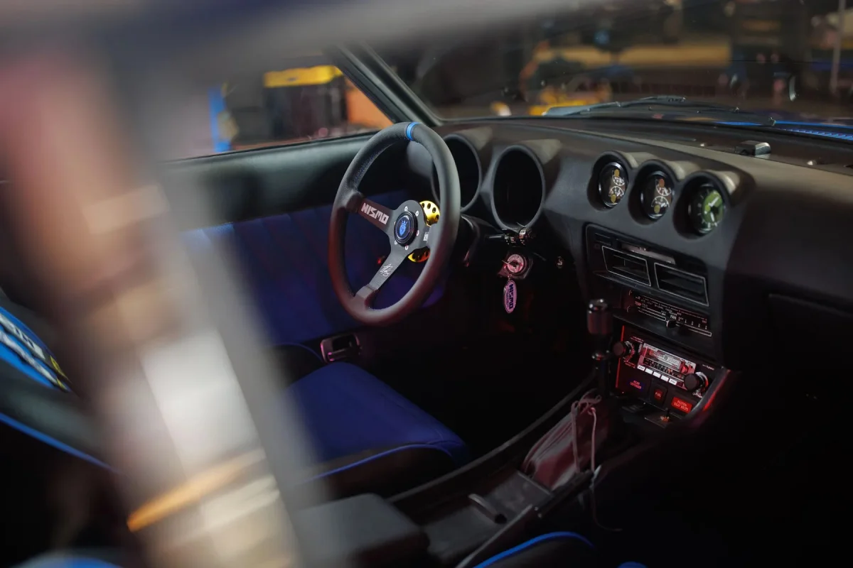 Vintage car interior featuring blue and black bucket seats and a Nismo steering wheel.