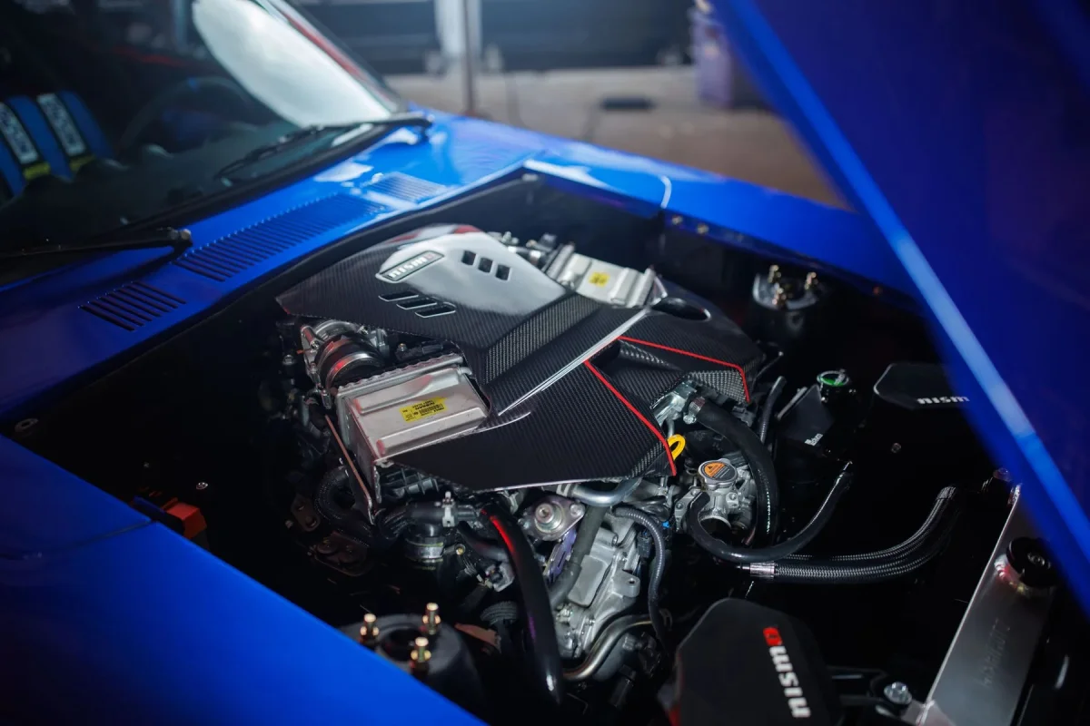 High-performance Nissan engine featuring a carbon fiber cover, visible inside the open hood of a bright blue car.