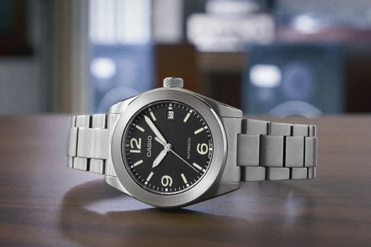 Casio automatic wristwatch featuring a black dial, Arabic numerals at the 6 and 12 o’clock positions, and a stainless steel link bracelet.