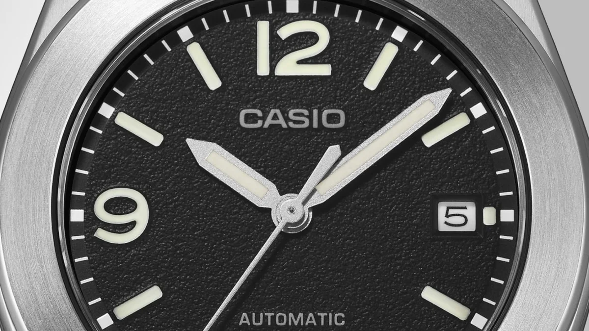 Casio automatic watch face in a close-up view, featuring a textured black dial, white numeral hour markers at 12 and 9, and a date window at the 3 o’clock position.