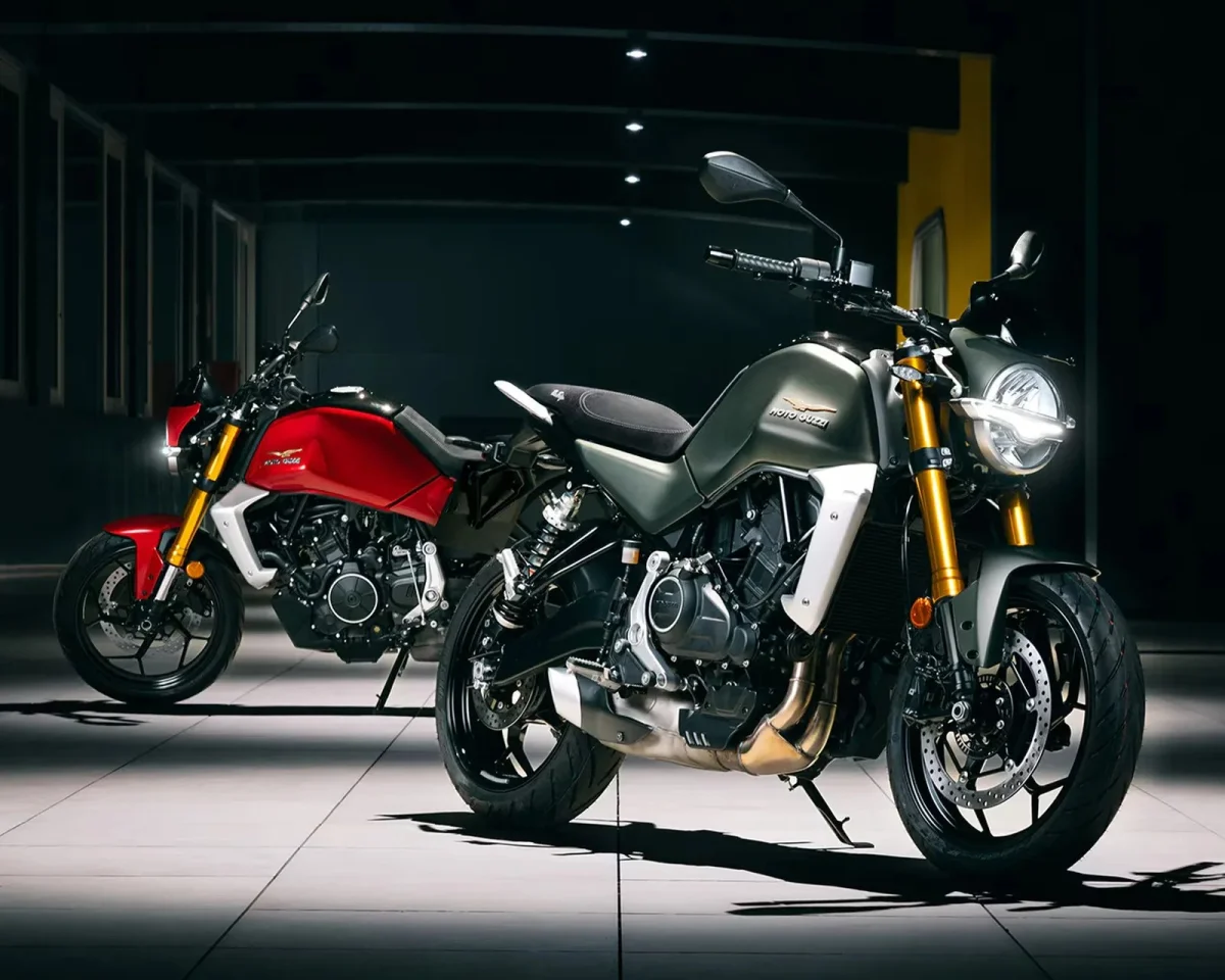 Two Moto Guzzi motorcycles parked indoors, one in olive green and one in red.
