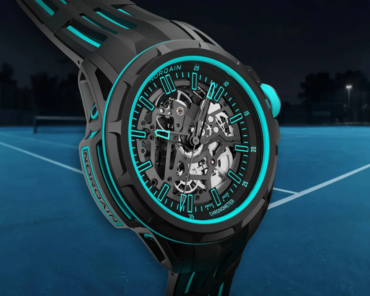 Norqain skeletonized watch featuring a black case and vibrant turquoise accents, displayed against a tennis court background.
