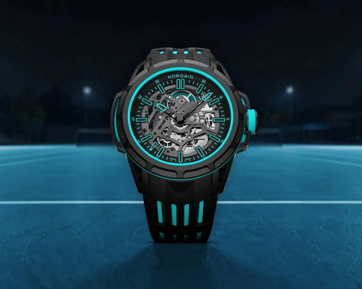 Norqain skeletonized watch featuring a black case and vibrant turquoise accents, displayed on a tennis court.