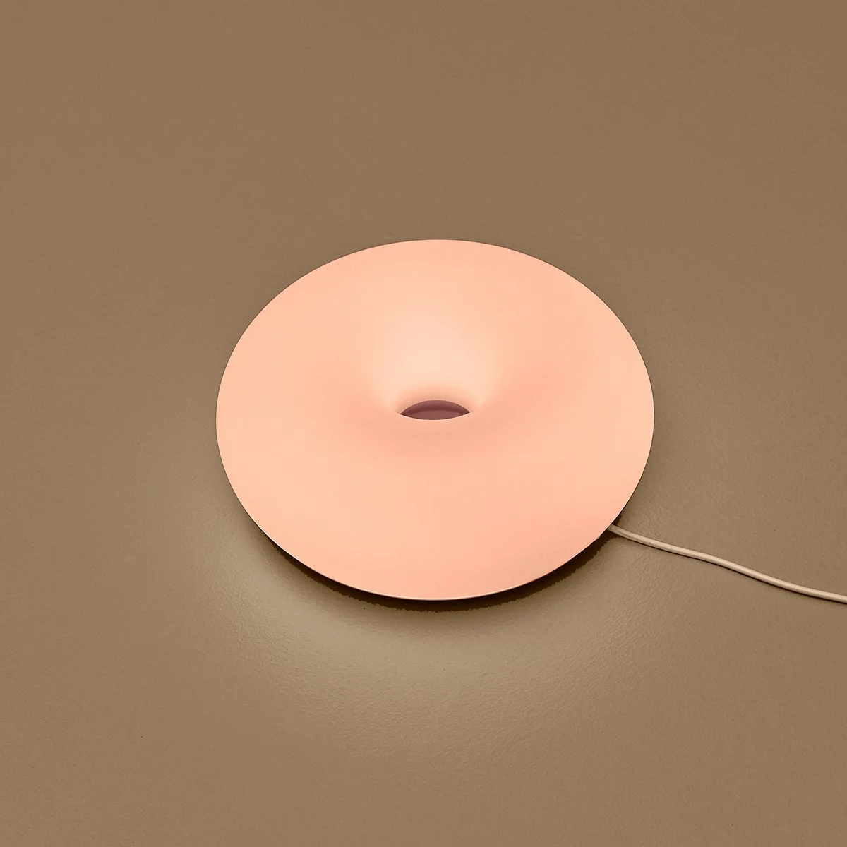 Round peach-colored donut-shaped lamp with a central hole on a brown surface.