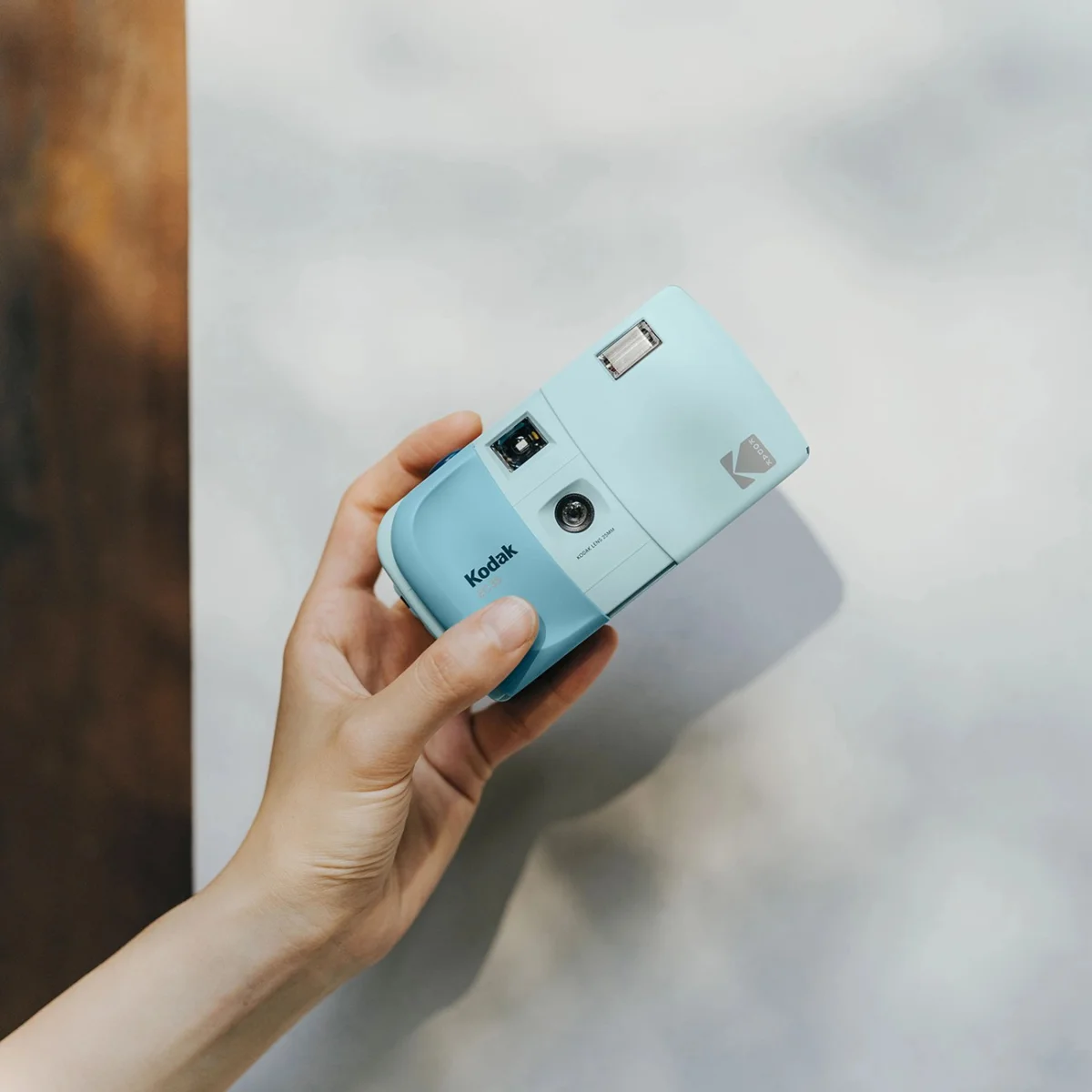 Hand holding a light blue Kodak instant camera with a flash and lens visible.