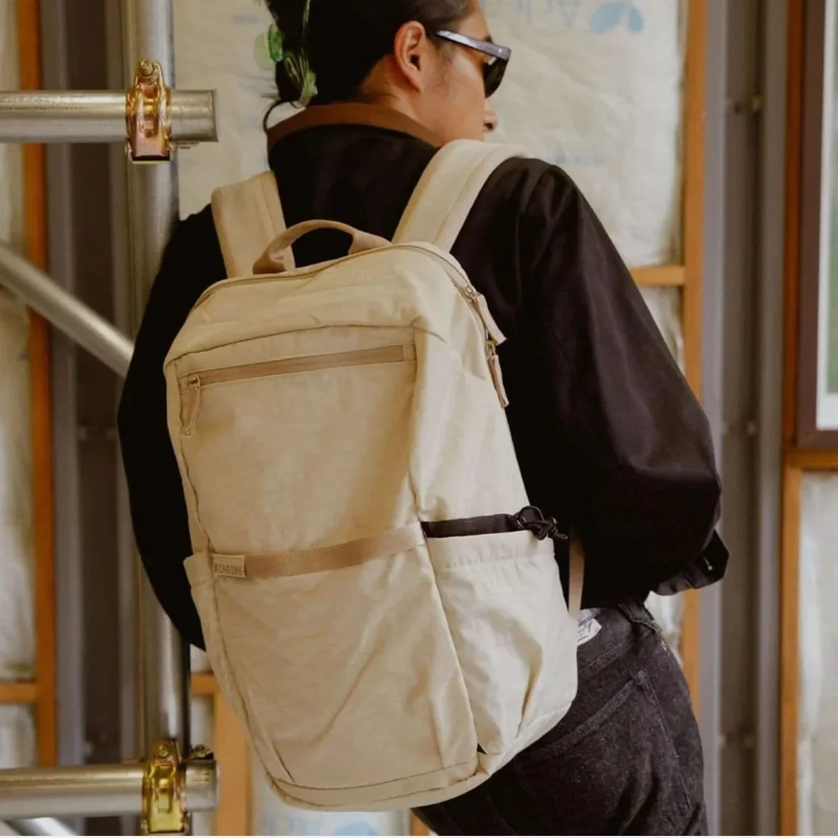 Beige backpack featuring a front zipper pocket and a small logo tag.