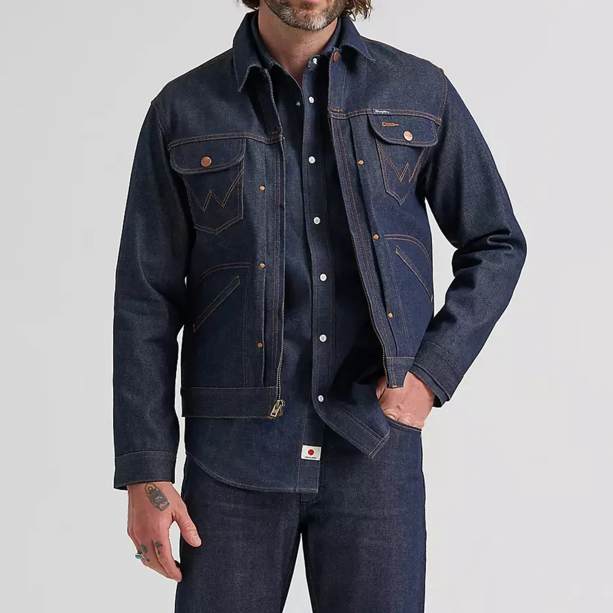 Dark denim jacket layered over a denim shirt and jeans, with one hand in a pocket; face partially out of frame.