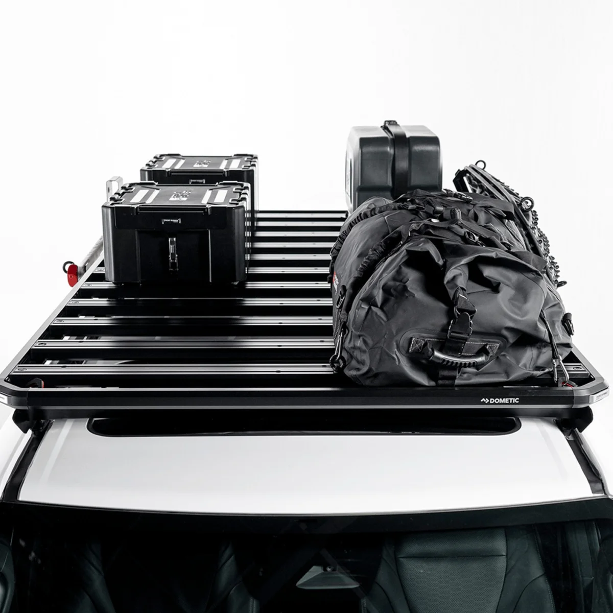Black metal roof rack loaded with two black storage boxes, a black duffel bag, and a black case on a white vehicle roof.