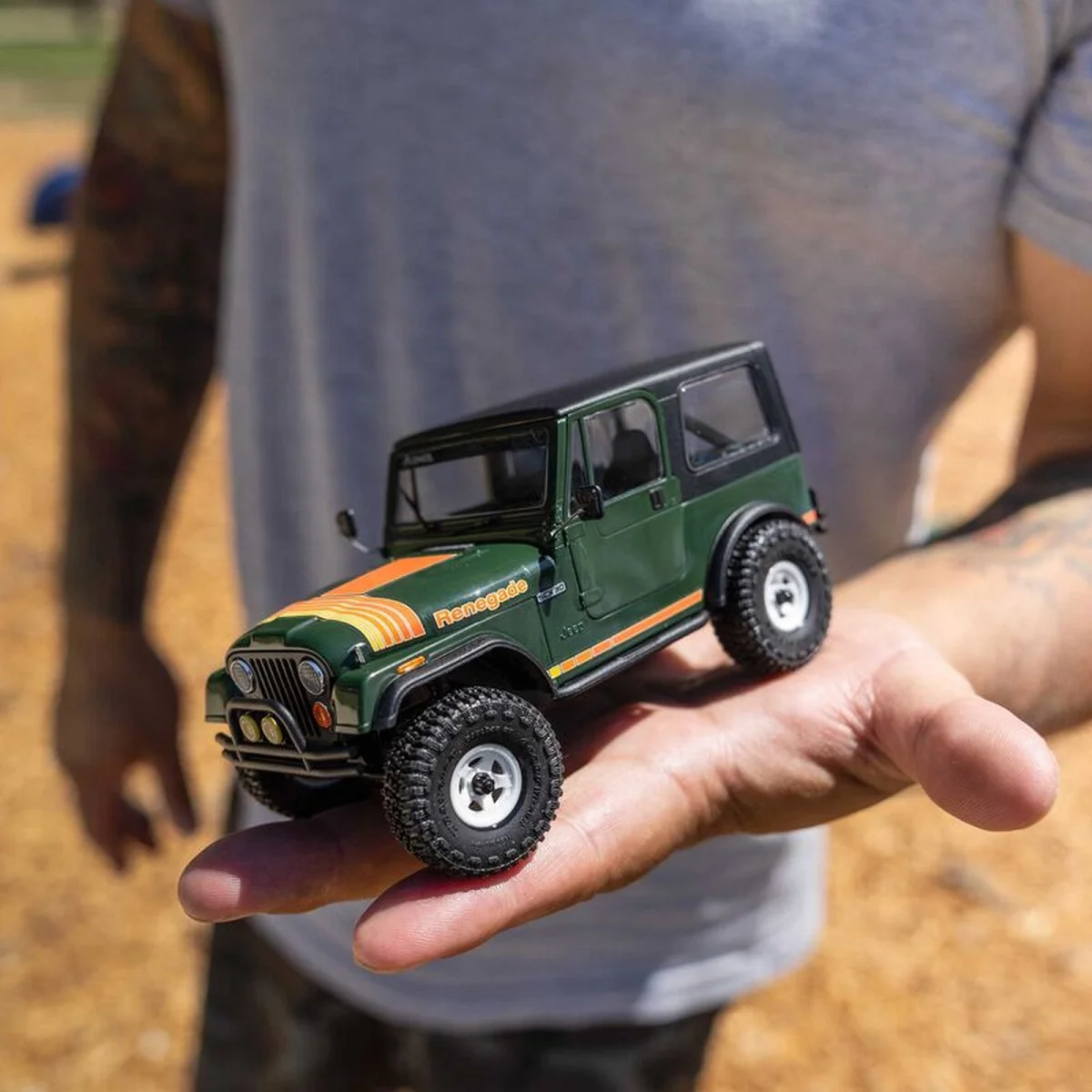Small, dark green model Jeep Renegade with orange and yellow hood stripes held in a hand.