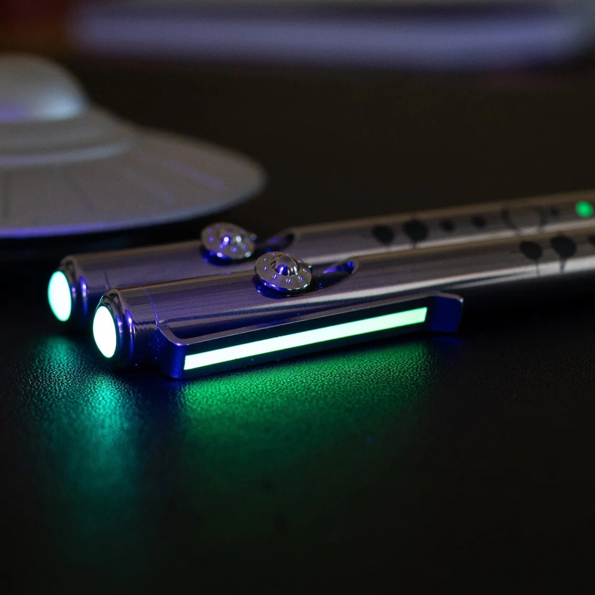 Two metallic lightsabers with glowing green blades resting on a dark surface.