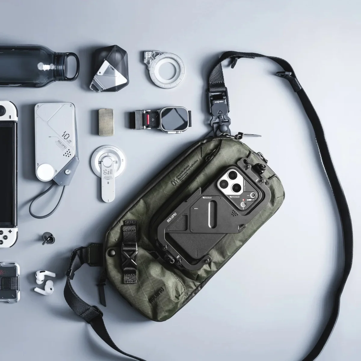 Green crossbody bag with black strap and a smartphone in a black rugged case attached on a gray surface.