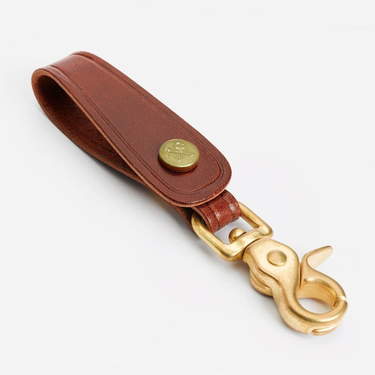 Brown leather key fob featuring a brass trigger snap hook and a brass stud with an anchor and hammer logo.