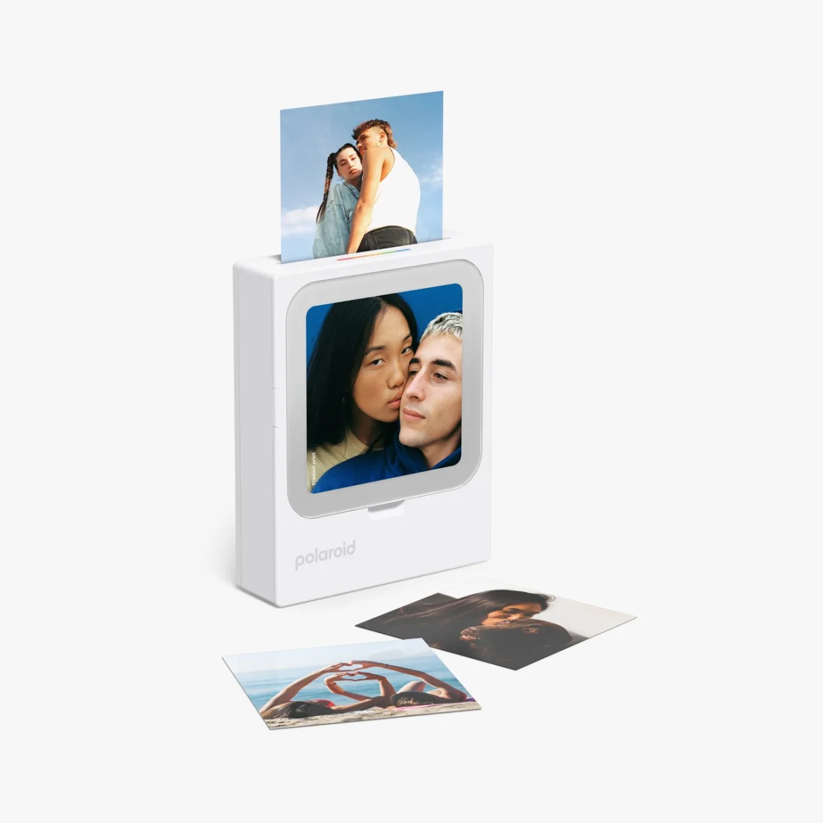 White Polaroid photo printer with a printed photo coming out and three printed photos lying in front.