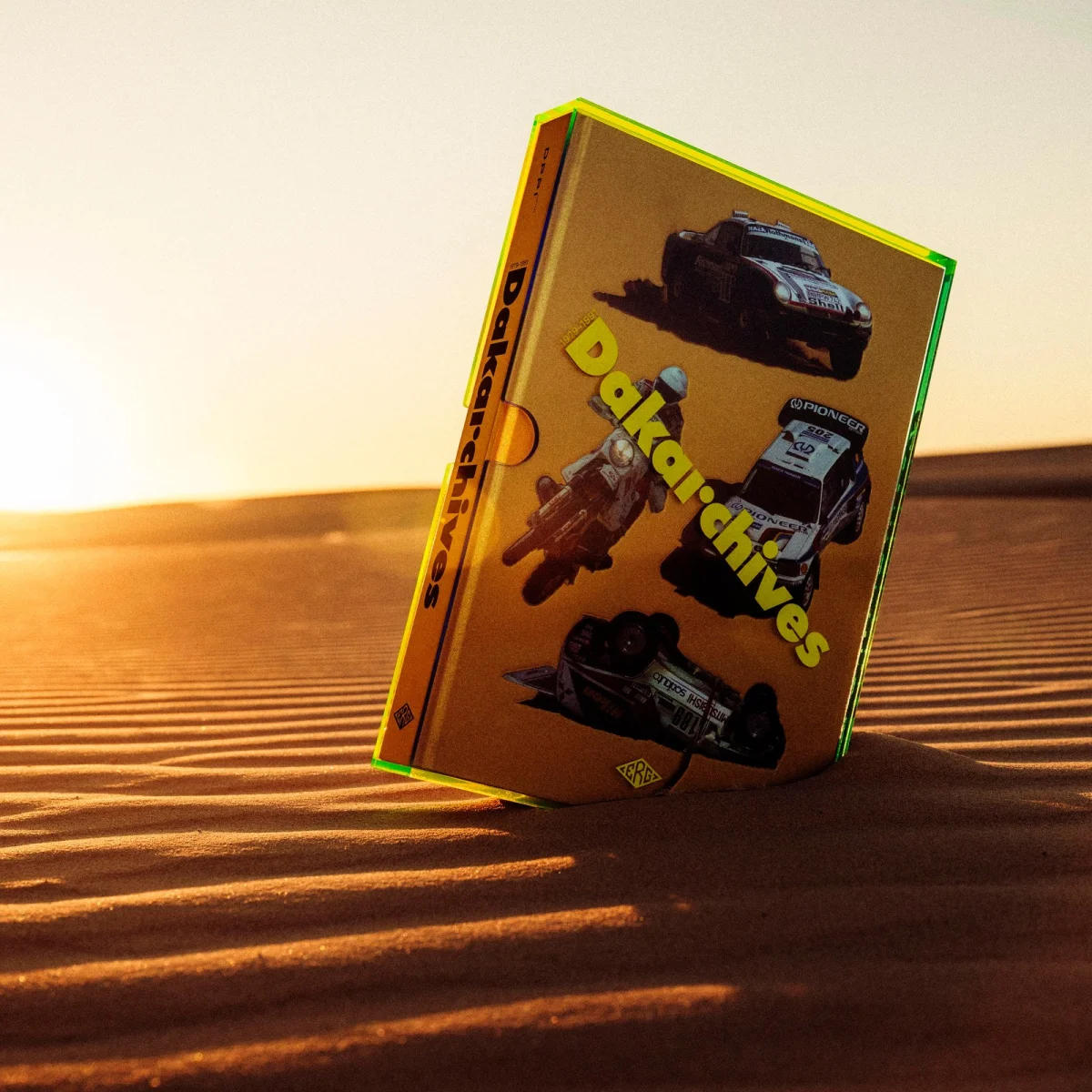 Yellow Dakararchives VHS tape featuring rally car images, standing upright on sand dunes at sunset.