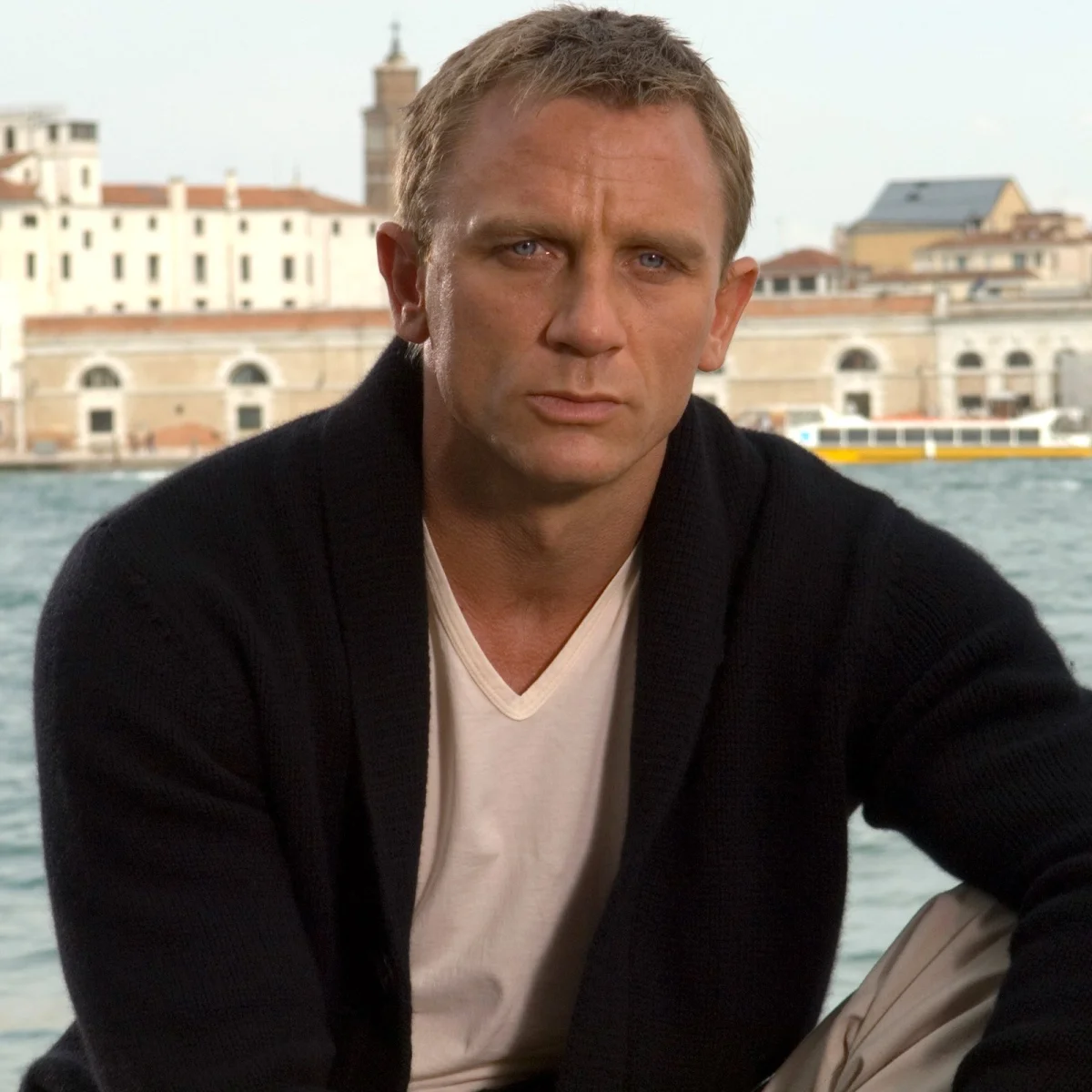 Dark navy shawl-collar cardigan worn over a white v-neck shirt, shown against a waterfront city skyline.