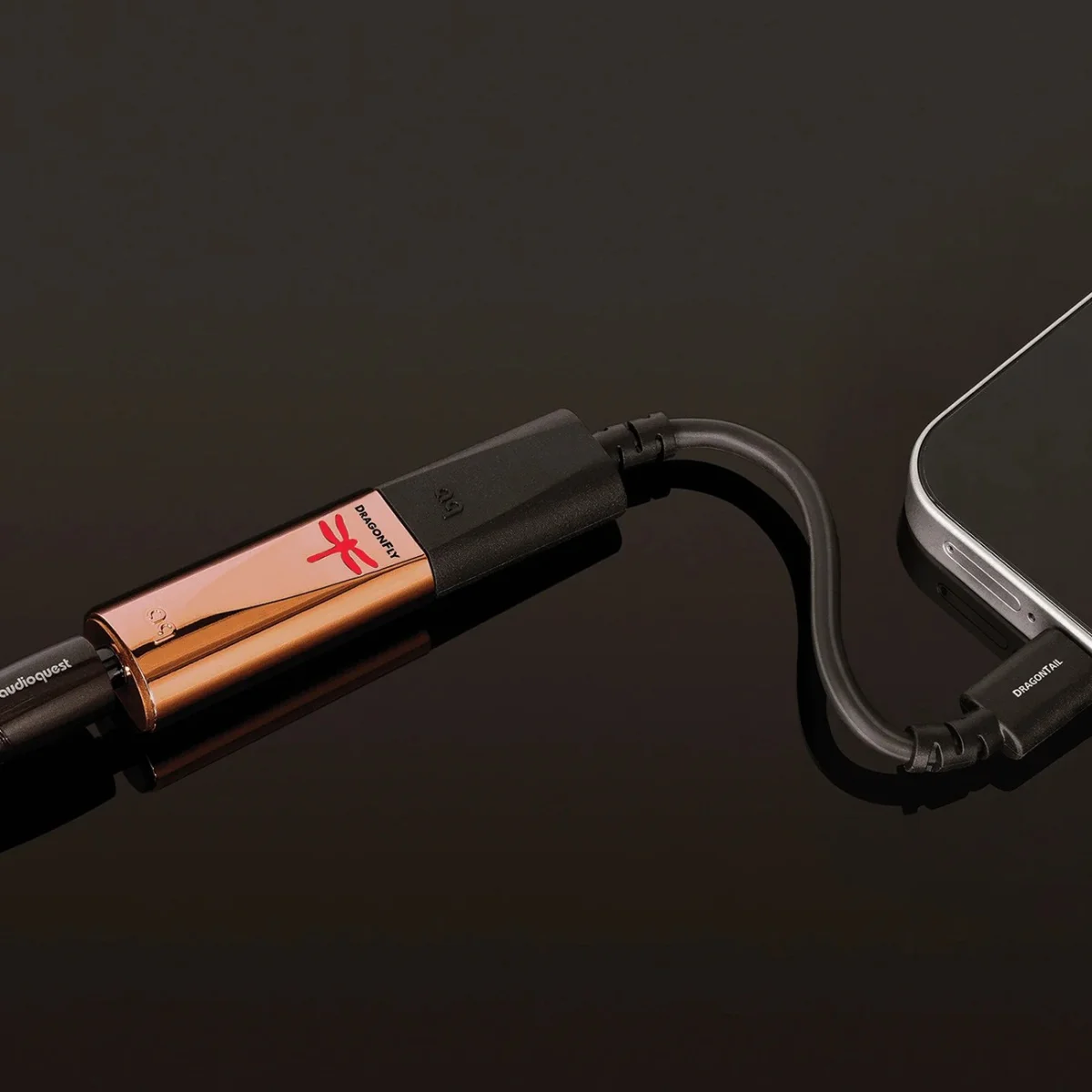Copper-colored DragonFly USB digital-to-analog converter connected to a smartphone via a short black cable labeled "DRAGONTAIL.