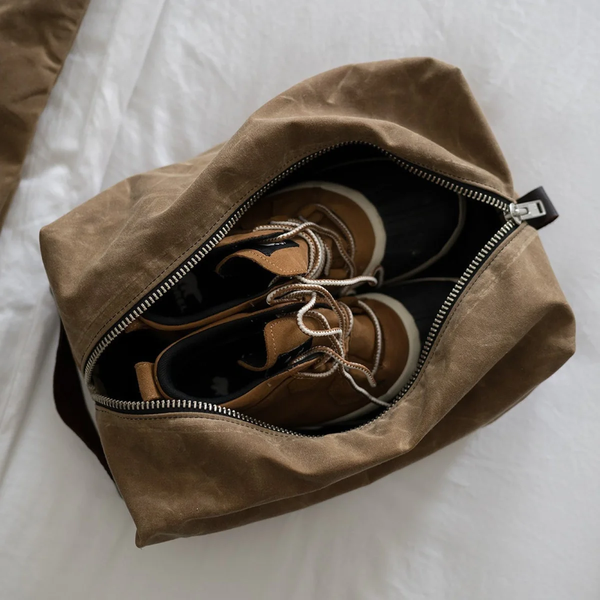 Tan and black lace-up boots inside an open brown zippered travel bag.
