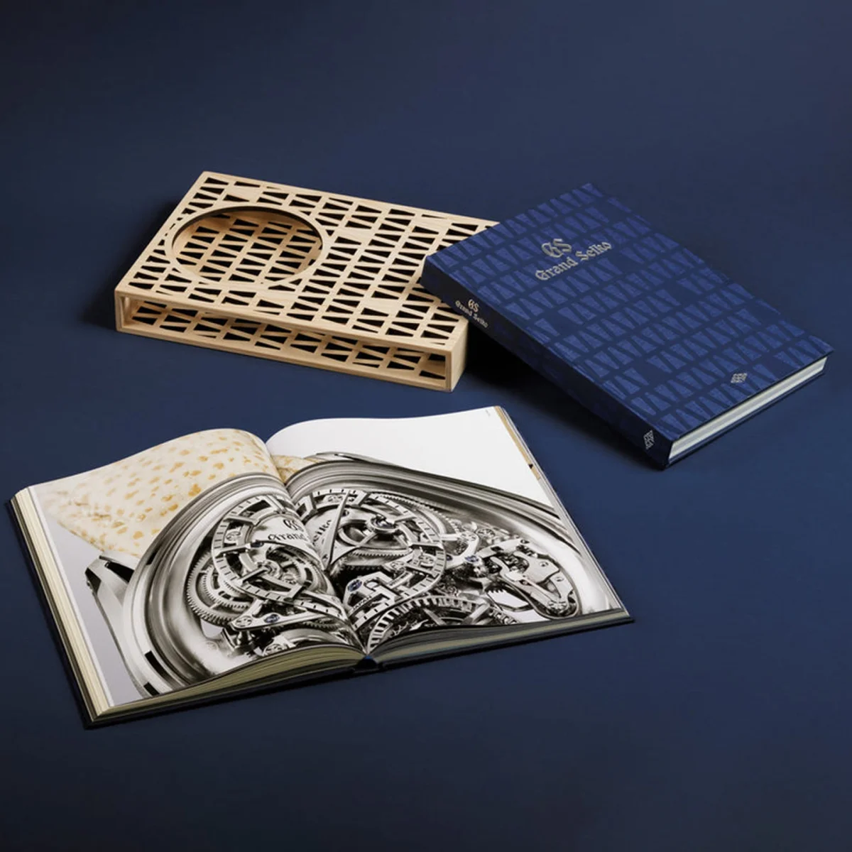 Blue hardcover book titled "Grand Seiko" with a wooden lattice book holder and an open book showing a detailed watch mechanism.