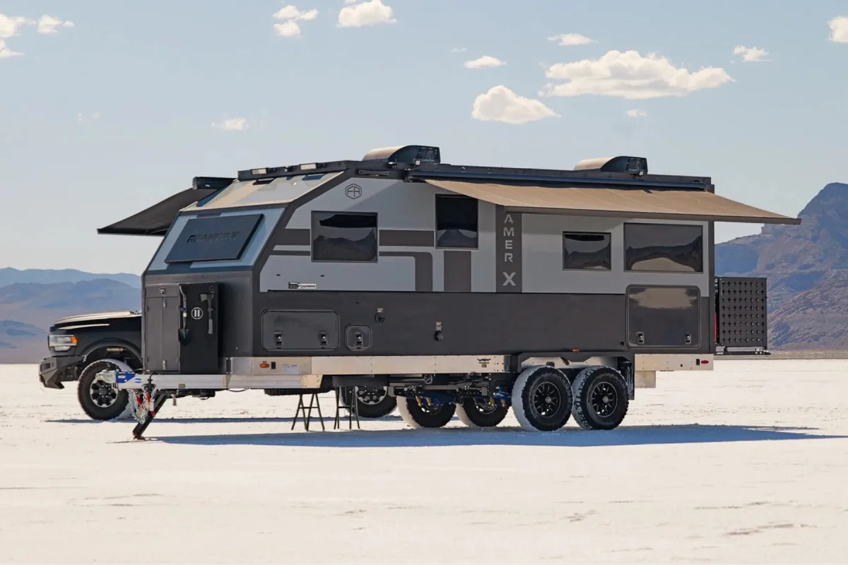 Grey and black off-road travel trailer with an extended awning parked on a salt flat, hitched to a truck.