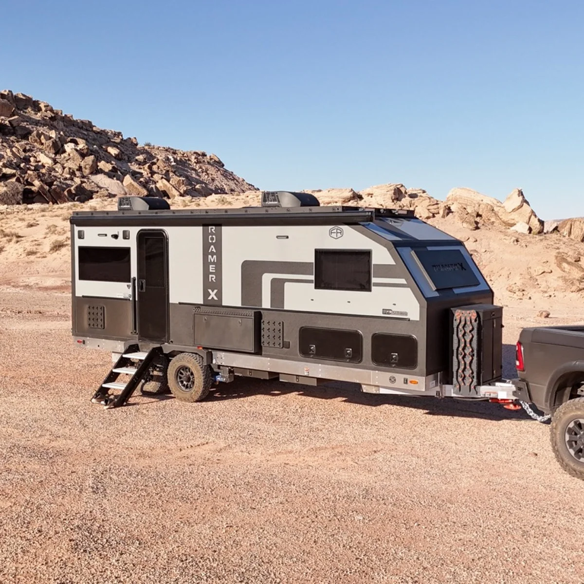Grey and black Roamer X off-road travel trailer hitched to a truck in a desert landscape.