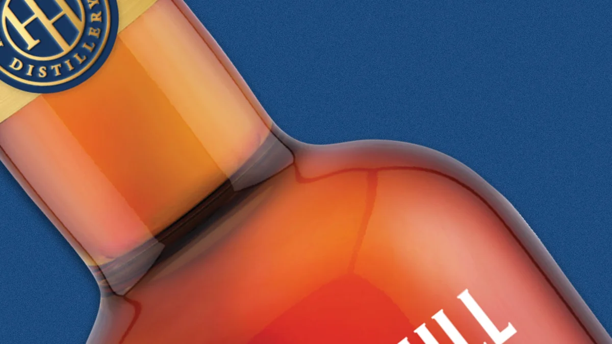 Close-up of a glass bottle filled with amber liquid, featuring a circular blue and gold distillery logo on the neck.