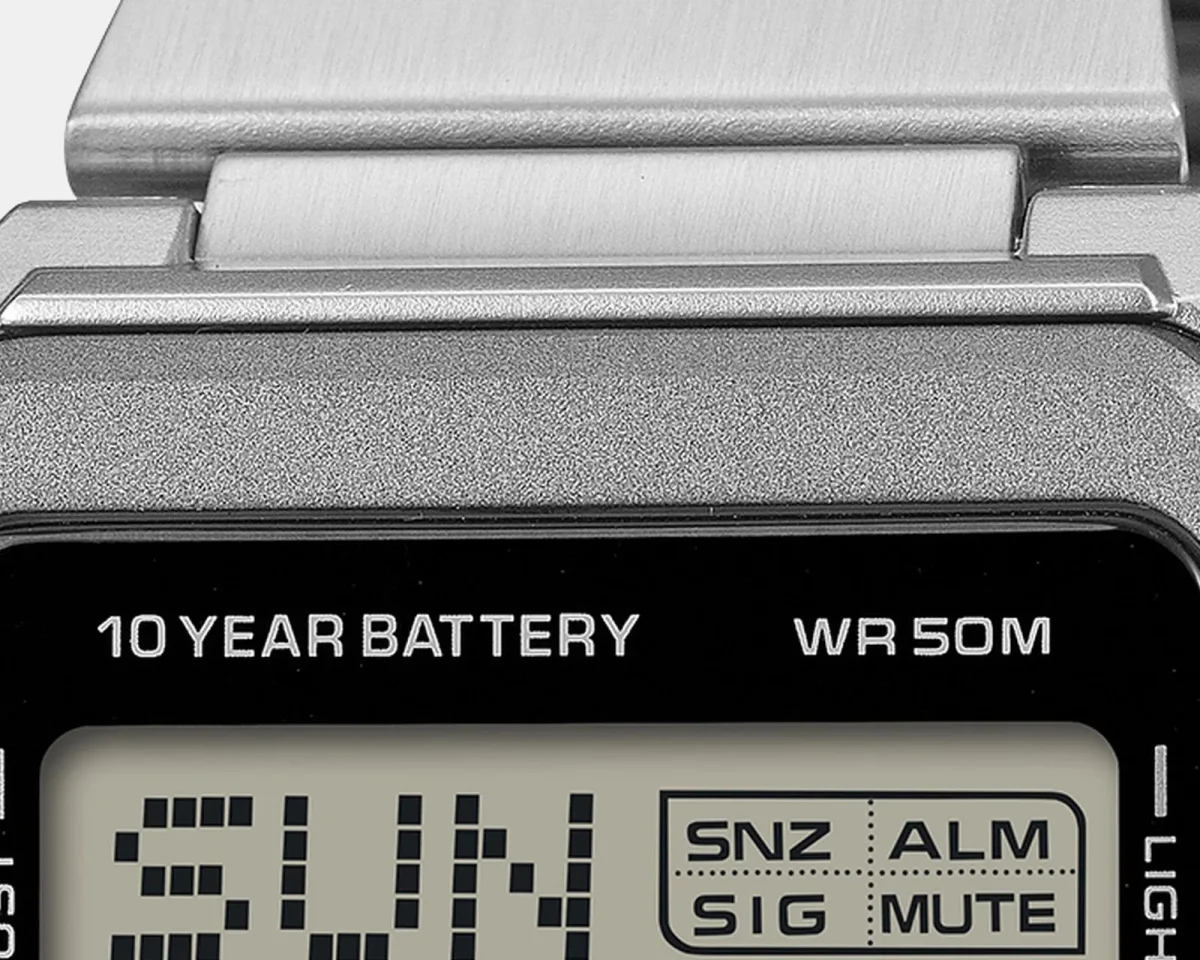 Close-up of a metallic digital watch face displaying 10 YEAR BATTERY and WR 50M, featuring a screen that shows SUN and indicator boxes for snooze, alarm, signal, and mute settings.