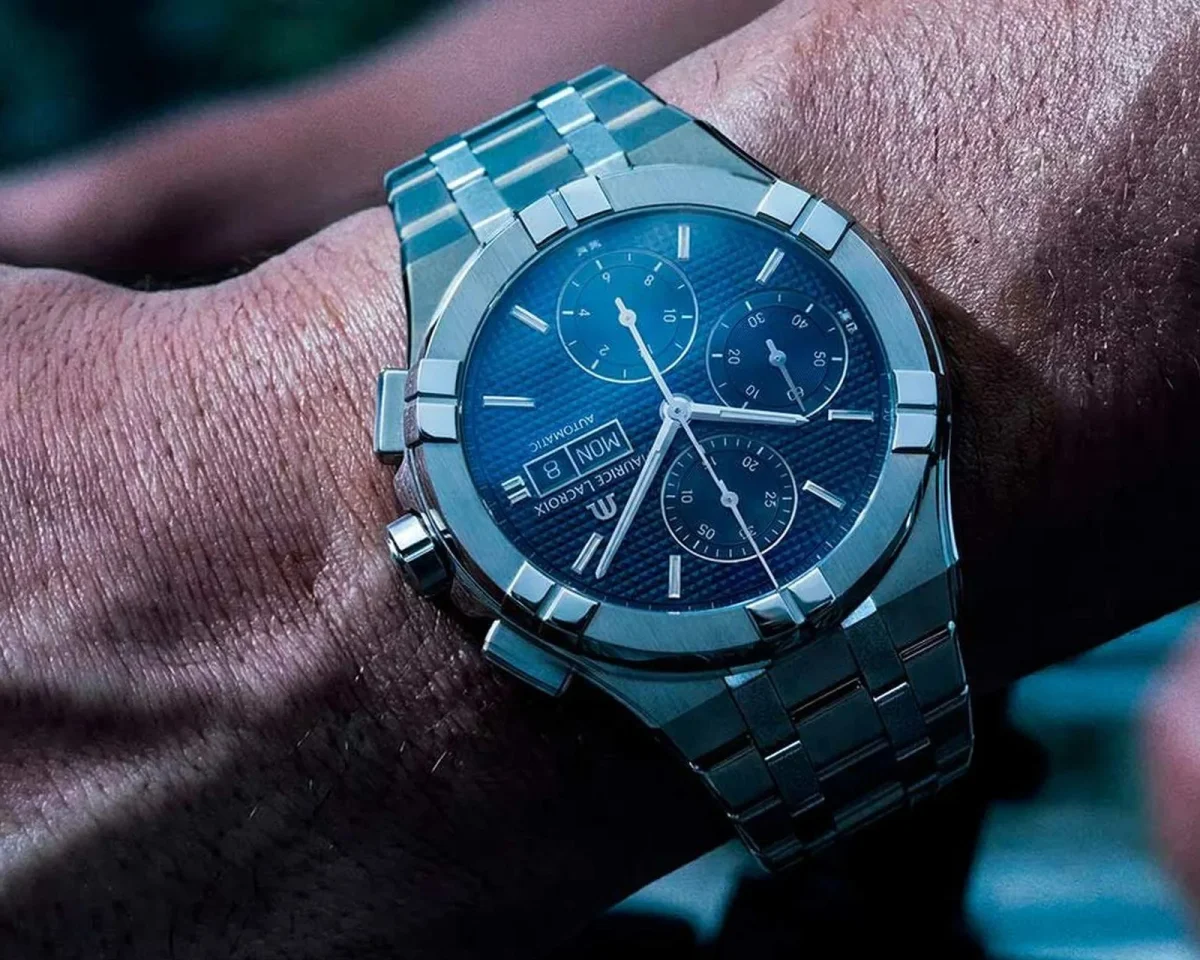 Maurice Lacroix Aikon chronograph watch featuring a blue textured dial and silver-tone metal link bracelet, shown on a wrist.